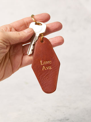 Tan leather keyring with gold lettering, hotel inspired Art Deco shape, with 'Love Ava' written on it.