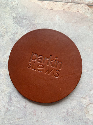A round, brown leather coaster with the engraved text 'PARKIN & LEWIS' in the center.