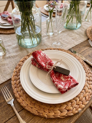 Set table with white plates, red floral napkins, and woven placemats on a wooden table, with olive green leather label stamped with Grandad
