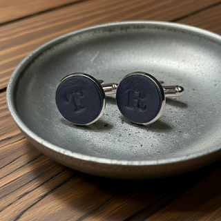 Navy blue cufflinks with silver trim on a textured gray dish.