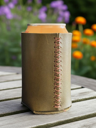 olive leather can cooler with a can on a wooden surface with a blurred floral background, close up of stitching