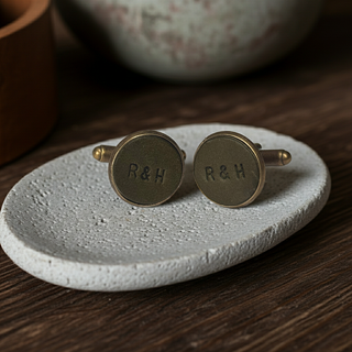 Pair of olive green bronze cufflinks with 'R&H' engraving on a textured stone coaster.