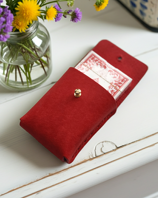Red card holder with pack of cards on a white surface with a vase of flowers.