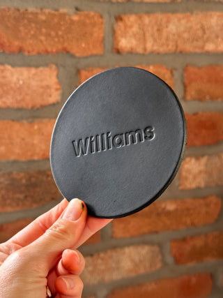 Round black lid with 'Williams' branding held in front of a brick wall.