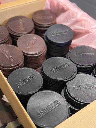 Stacks of Ashmore branded round objects in a box with a pink plastic bag.
