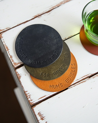blue, green and yellow coaster, hand stamped with personalised message lying on a wooden table.