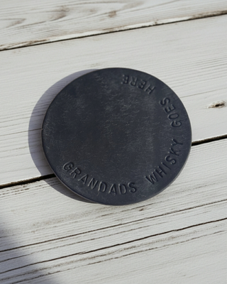 navy blue coaster stamped with 'grandads whisky goes here' on a white wooden table.