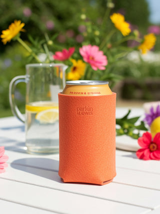 Pink can cooler with 'Parkin & Lewis.' branding on a table with flowers and lemonade in the background.